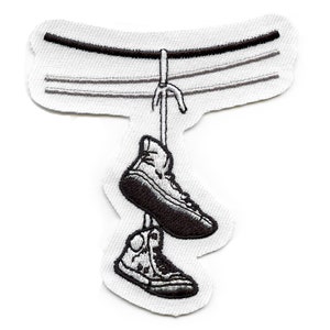 May include: A white embroidered patch of two black and white sneakers hanging from a black wire.