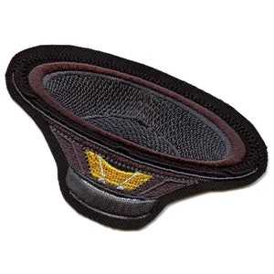 Puede incluir: Un parche bordado negro y gris con forma de altavoz. El altavoz tiene un centro amarillo con un diseño estilizado.