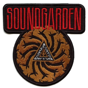 May include: A black and brown embroidered patch with the band name "SOUNDGARDEN" in red lettering above a brown and black swirling design with a white triangle in the centre.