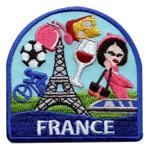Könnte beinhalten: Ein blauer und weißer gestickter Aufnäher mit dem Wort "FRANCE" in weißen Buchstaben. Der Aufnäher zeigt einen Cartoon-Eiffelturm, einen Fußball, ein Fahrrad, ein Glas Wein, ein Stück Käse und eine Frau in einem rosa Kleid.