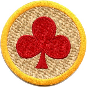 May include: A red embroidered clover on a beige background with a yellow border. The clover is a common symbol of good luck.