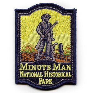 Peut inclure: Un écusson brodé bleu et jaune représentant un personnage historique tenant un fusil. Le texte "MINUTE MAN NATIONAL HISTORICAL PARK" est affiché sous la figure.