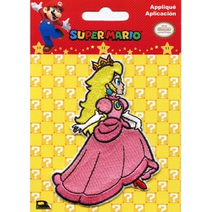Puede incluir: Parche para planchar con la Princesa Peach de la serie de videojuegos Super Mario. El parche es rosa y blanco con un fondo amarillo. El texto "SUPER MARIO" está impreso en el embalaje.