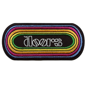 May include: A black and white embroidered patch with the words "The Doors" in a rainbow of colors. The patch is oval shaped and has a black background.