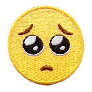 Könnte beinhalten: Gelber gestickter Bügelaufkleber mit einem traurigen Emoji-Gesicht. Das Emoji hat große, runde Augen mit schwarzen Pupillen und weißen Highlights. Die Augenbrauen sind gewölbt und der Mund ist eine dünne, gebogene Linie.