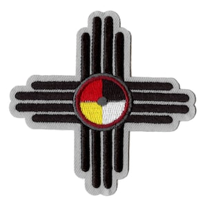 May include: A grey embroidered patch featuring a black and white Zia sun symbol. The symbol is a circle with four colours: red, yellow, white, and black. The symbol is surrounded by eight rays.