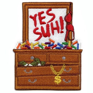 Pode incluir: Um remendo bordado que representa uma cômoda com um espelho que diz "YES SUH!" em letras vermelhas. A gaveta superior está cheia de itens coloridos, a gaveta do meio contém itens verdes e a gaveta inferior tem uma corrente dourada com um sinal de dólar.