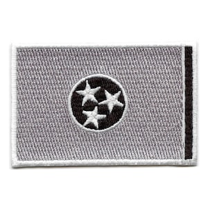 May include: A white embroidered patch featuring a black circle with three white stars, representing the state of Tennessee. The patch has a black border on the right side.