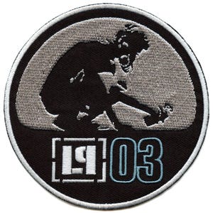 May include: A black and white embroidered patch featuring a silhouette of a person in a crouching position. The patch has the text "[ ] 03" in white and blue.