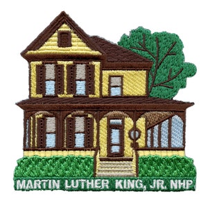 Puede incluir: Parche bordado que representa una casa amarilla con detalles marrones y un árbol verde. La casa tiene un porche con columnas marrones y una puerta blanca. El texto "MARTIN LUTHER KING, JR. NHNP" está en la parte inferior del parche.
