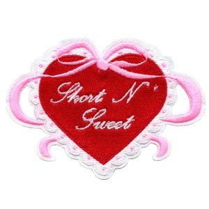 Puede incluir: Parche bordado en forma de corazón rojo con ribete de encaje blanco y lazos de cinta rosa. El texto "Short N' Sweet" está bordado en blanco sobre el corazón.