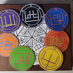 May include: A set of nine circular, colorful stickers with various symbols and text. The stickers are arranged in a circle around a larger, white circle with black text and symbols. The text on the stickers includes "PHUL", "BETHOR", "A", "B", "Φ", "Ω", and "H".