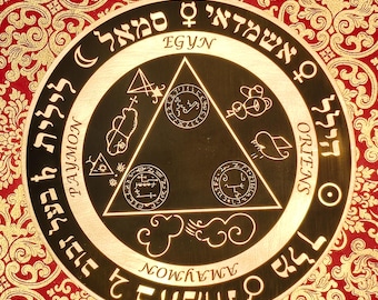 May include: A circular, gold-colored talisman with intricate symbols and text in a foreign language. The center features a black triangle with additional symbols. The background is a red and gold patterned fabric.