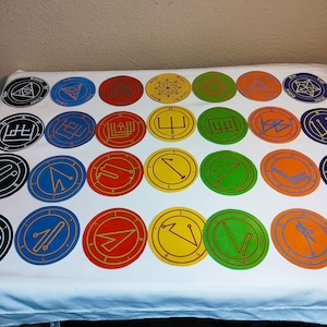 Puede incluir: Veinticuatro posavasos redondos y coloridos con diferentes símbolos dibujados en blanco y amarillo. Los posavasos están dispuestos en cuatro filas de seis.