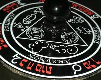 Pode incluir: Um altar oculto preto e branco com letras e símbolos vermelhos. Uma bola de cristal preta está sobre um suporte decorativo no centro. O altar apresenta os nomes "PAYMON" e "ORIENTS".
