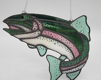 May include: Stained glass rainbow trout with green, pink, and white sections. The fish has black dotted details and is suspended by a silver chain. The trout is a decorative item.