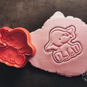 Könnte beinhalten: Zwei Elefanten-Ausstecher, einer rot und einer rosa. Der rote Ausstecher ist eine detaillierte Umrandung eines Elefanten mit einem Herz auf dem Kopf. Der rosa Ausstecher ist ein Abdruck des Elefanten in rosa Knetmasse.