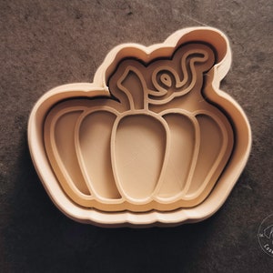 Puede incluir: Un cortador de galletas de calabaza de pl&aacute;stico beige con un tallo y nervaduras detalladas.