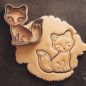 Könnte beinhalten: Ein Ausstecher in Form eines Fuchses auf einer braunen Oberfläche. Der Ausstecher ist aus Metall und hat ein detailliertes Design. Der Ausstecher wird verwendet, um eine Fuchsform aus einem Stück Teig auszustechen.