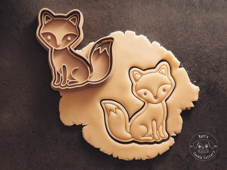 Puede incluir: Un cortador de galletas con forma de zorro sobre una superficie marr&oacute;n. El cortador est&aacute; hecho de metal y tiene un dise&ntilde;o detallado. El cortador se est&aacute; utilizando para cortar una forma de zorro de una pieza de masa.