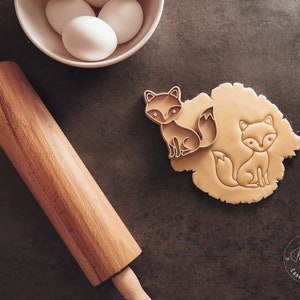 Puede incluir: Dos cortadores de galletas con forma de zorro sobre una superficie marr&oacute;n. Un cortador est&aacute; encima de una masa, el otro est&aacute; al lado. Un rodillo de madera y un taz&oacute;n de huevos est&aacute;n en el fondo. La imagen incluye el texto "Karl's Cookie Cutters".