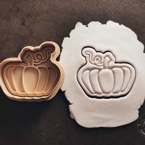 Puede incluir: Un cortador de galletas con forma de calabaza. El cortador est&aacute; hecho de pl&aacute;stico marr&oacute;n y tiene un dise&ntilde;o detallado. El cortador est&aacute; sobre una superficie blanca.