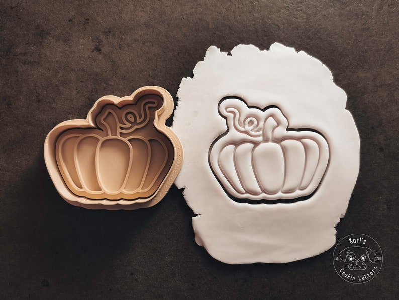 Puede incluir: Un cortador de galletas con forma de calabaza. El cortador est&aacute; hecho de pl&aacute;stico marr&oacute;n y tiene un dise&ntilde;o detallado. El cortador est&aacute; sobre una superficie blanca.
