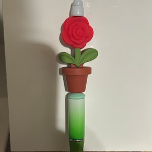 May include: A red rose with green leaves and a brown pot on top of a green and red gradient pen.