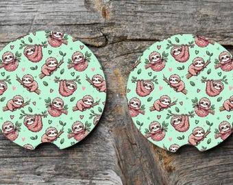 May include: Two round coasters with a green background and a repeating pattern of pink sloths hanging from branches with green leaves.