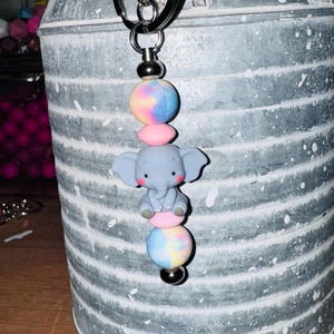 May include: A gray elephant charm with pink and blue tie-dye beads on a silver keychain.
