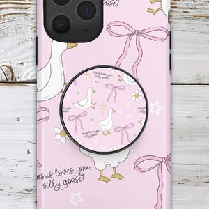 May include: Pink phone case with a whimsical design featuring white geese, pink bows, daisies, and stars. The case includes the text "Jesus loves you, silly goose!" and a matching pop socket.