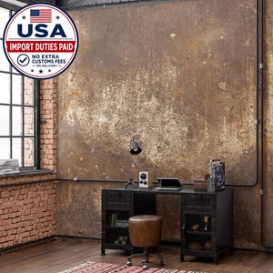 May include: A black metal desk with two storage cabinets featuring mesh doors, a matching brown leather stool, a small desk lamp, a laptop, and a book. The desk is positioned against a textured, weathered brown wall with exposed brick and pipes.