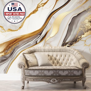 Puede incluir: Un sofá beige capitoné con brazos curvos y cojín de asiento estampado, colocado frente a un mural de pared con un diseño abstracto fluido de vetas de mármol blanco, gris y dorado con acentos de oro metálico en todo el patrón.