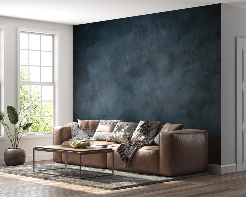 May include: A dark navy blue wall with a textured, mottled finish behind a low-profile brown leather sofa. The sofa is adorned with several patterned throw pillows and a draped blanket, positioned on a gray area rug with a wooden coffee table.
