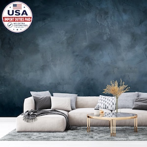 May include: A dark blue wall with a textured, mottled finish behind a light beige sectional sofa. The sofa features several gray and white throw pillows. A round coffee table with a gold frame and glass top sits on a gray rug in front of the sofa.