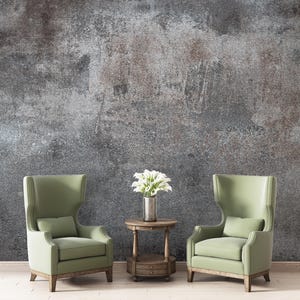 May include: Two light green wingback chairs with matching pillows flank a small wooden side table. A vase of white flowers sits on the table. The background is a textured gray wall.