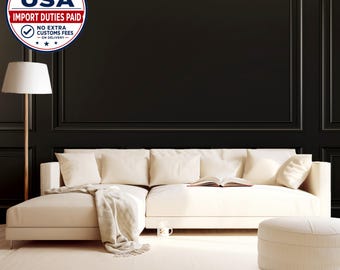 May include: A cream-colored sectional sofa with a chaise lounge, several matching throw pillows, and a draped throw blanket. A floor lamp with a white shade stands to the left, and a matching cream-colored ottoman sits in the foreground.