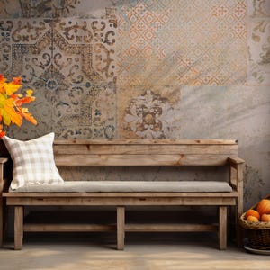 Op de afbeelding: Een rustieke houten bank met een lichtgrijze kussen zit voor een muur met een behang met patronen. Het behang heeft een patchwork van verschillende ontwerpen in tinten bruin, beige en blauw. Een boeket herfstbladeren ligt op de vloer links van de bank.