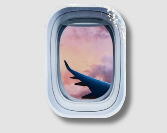 May include: A close-up of an airplane window with a view of a pink and purple sunset with a wing of the plane visible in the lower right corner.
