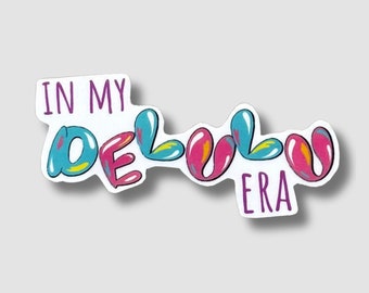 May include: A sticker with the text "In My Delulu Era" in a colourful, bubbly font. The letters are pink, blue, and yellow.