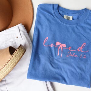 May include: A blue t-shirt with a pink ribbon and the words "loved" and "John 3:16" printed on it.