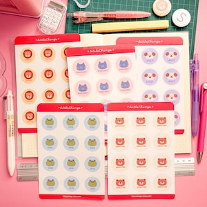 May include: Five sheets of circular stickers featuring animal illustrations and names including Tobias, Margaret, Leucy, Jose, and Sebastian. Each sheet is labelled with the text LittleChings. The stickers are arranged on a grid with various pens, a calculator, and a ruler.