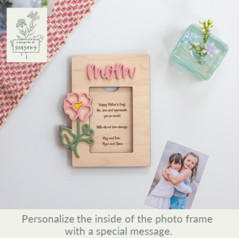 May include: Wooden photo frame with a pink flower cutout and the word "mom" on the top. The frame has a space for a photo and a personalized message inside. The message reads "Happy Mother's Day. We love and appreciate you so much. With all our love always. May and Dan, Maya and Olivia."