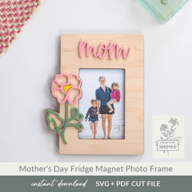 May include: A wooden photo frame with a pink flower design and the word "mom" on the top. The frame is designed to be a fridge magnet. The frame is for a 4x6 inch photo.