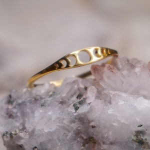 Peut inclure: Une bague en or avec un motif de croissant de lune repose sur un amas de cristaux blancs et roses. La bague est un bijou délicat avec un design simple et élégant.