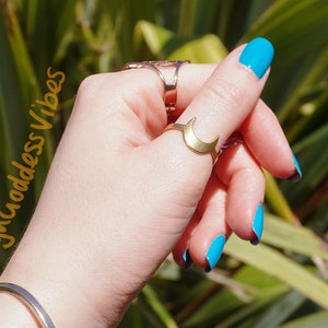 Può includere: Una mano che indossa un braccialetto rigido d'argento e diversi braccialetti di perline, tra cui un braccialetto di pietra bianca, un braccialetto di granato e un braccialetto di perline blu e nere. La mano indossa anche un anello d'oro con un design a forma di mezzaluna.