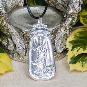 May include: Silver pendant necklace featuring a detailed depiction of a goddess figure. The pendant is attached to a black cord.