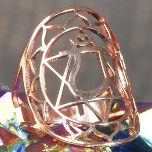 Può includere: Un anello in oro rosa con un delicato design traforato che presenta un simbolo di chakra stilizzato. L'anello è posto su uno sfondo di cristalli iridescenti.