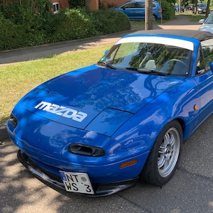 May include: A bright blue Mazda MX-5 convertible with a white racing stripe across the windscreen. The car has a black soft top and a black front bumper. The car has a number plate that reads "NT WS 3".