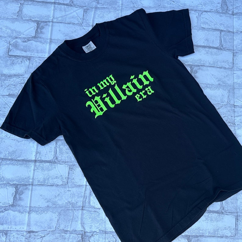 May include: Black t-shirt with green text that reads "in my Villain era".
